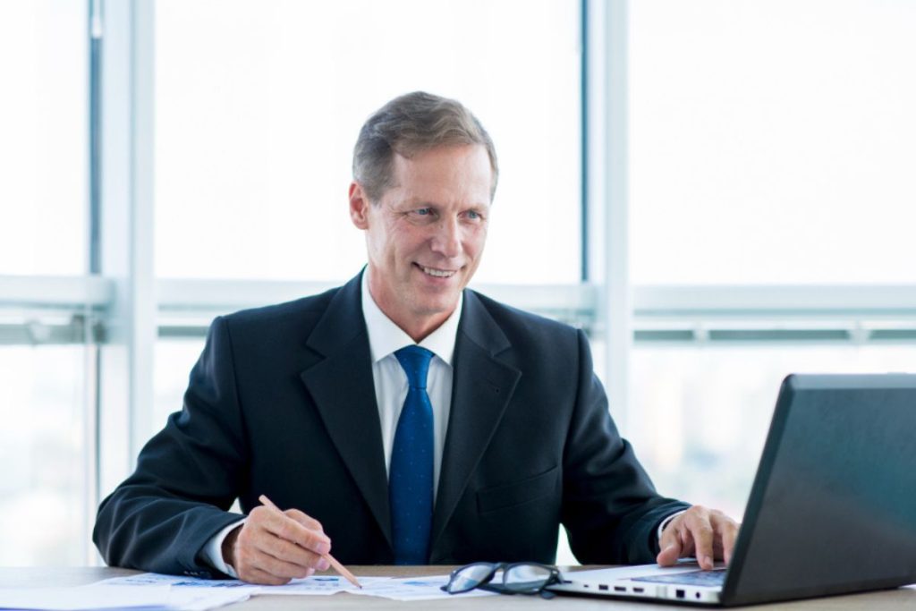 Advogado sorrindo, fazendo anotações e mexendo no notebook, representando um software jurídico gratuito.