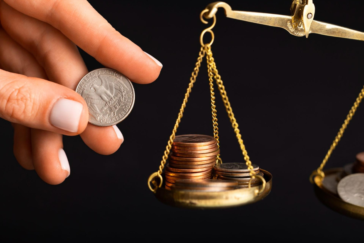 Mão segurando uma moeda enquanto a coloca em uma balança, representando um artigo da Business Company sobre fluxo de caixa do escritório de advocacia.