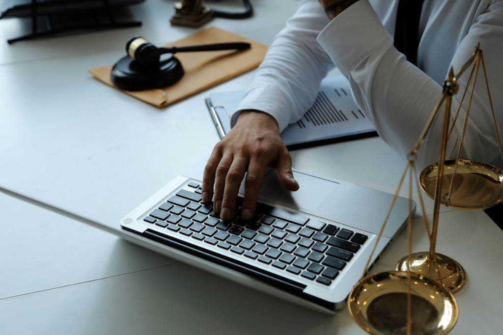 Vista de cima de rapaz usando um notebook sobre uma mesa, que também contém elementos jurídicos como balança e martelo, representando um artigo do Gojur sobre software jurídico completo.