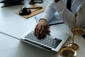 Vista de cima de rapaz usando um notebook sobre uma mesa, que também contém elementos jurídicos como balança e martelo, representando um artigo do Gojur sobre software jurídico completo.