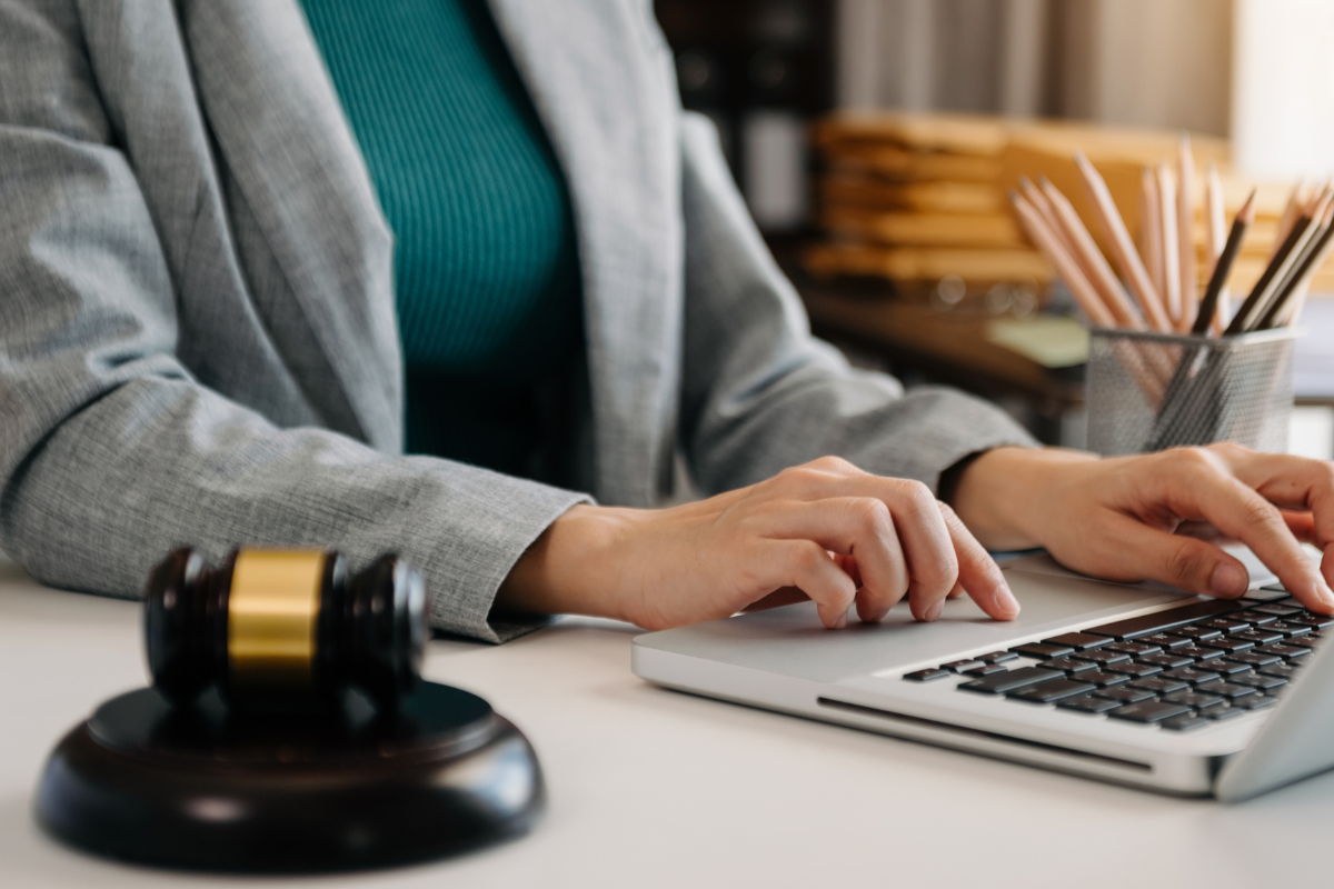 Mãos femininas digitando em um notebook, com um martelo de juiz ao lado, representando a advocacia 5.0 em um artigo do Gojur.