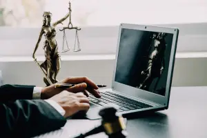 Advogado digita sobre um teclado de notebook apoiado em uma mesa com os símbolos da advocacia, ilustrando um artigo do GOJUR sobre o que é jurisprudência.